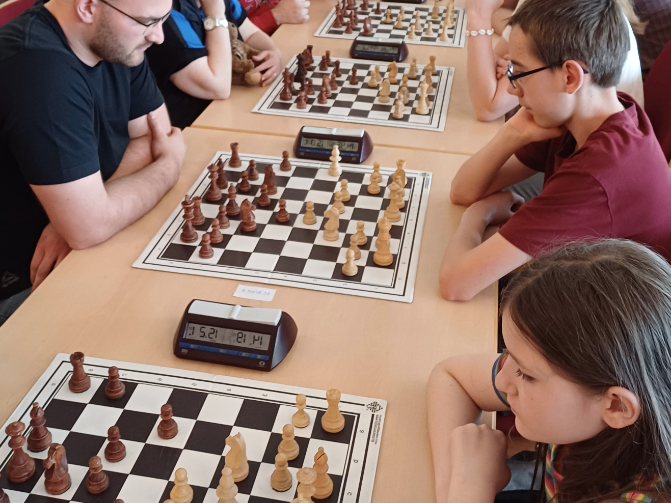 AI generated: The image shows several people playing chess at tables. Each table has a chessboard and a chess clock while the players are concentrating on their thoughts.