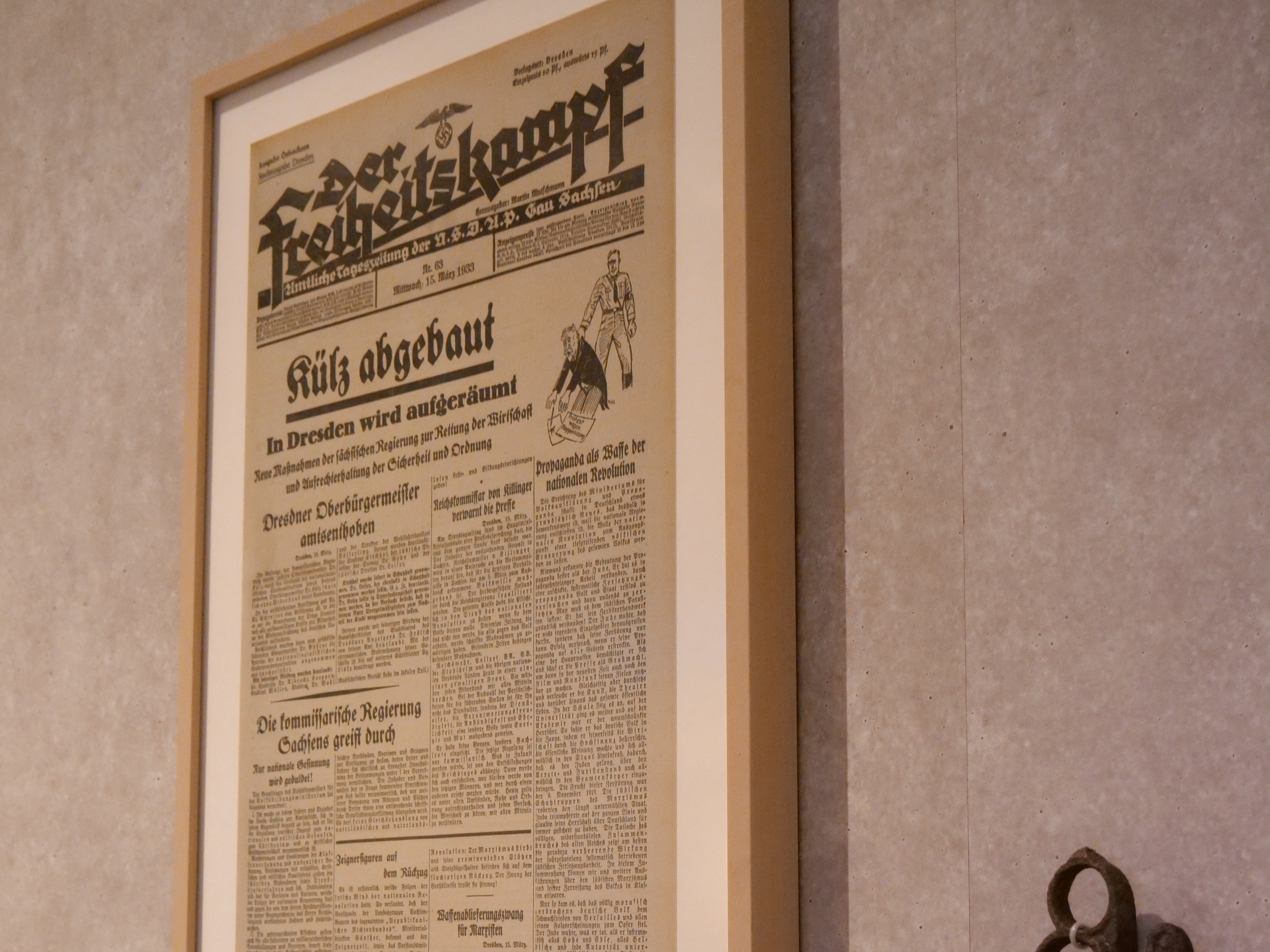 KI generiert: Das Bild zeigt eine gerahmte Zeitungsausgabe an einer Ausstellungswand, daneben ist ein Schlagring zu sehen. Unterhalb der Zeitung befinden sich erklärende Textelemente zur historischen Kontextualisierung.