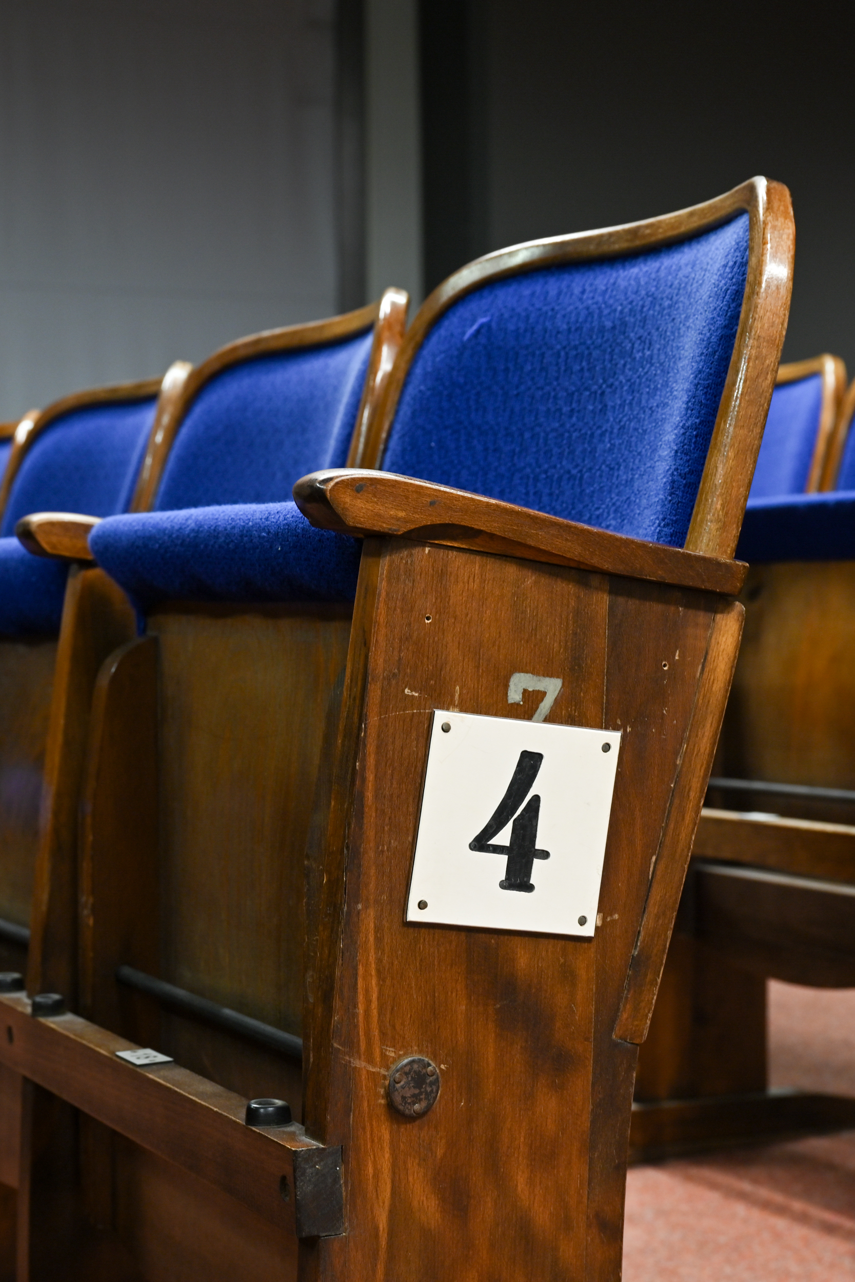KI generiert: Das Bild zeigt eine Reihe von Holztheatersitzen mit blauen Polstern, wobei einer der Sitzplätze mit der Nummer 4 gekennzeichnet ist. Die Sitze sind in einer Reihe angeordnet und wirken klassisch und gepflegt.