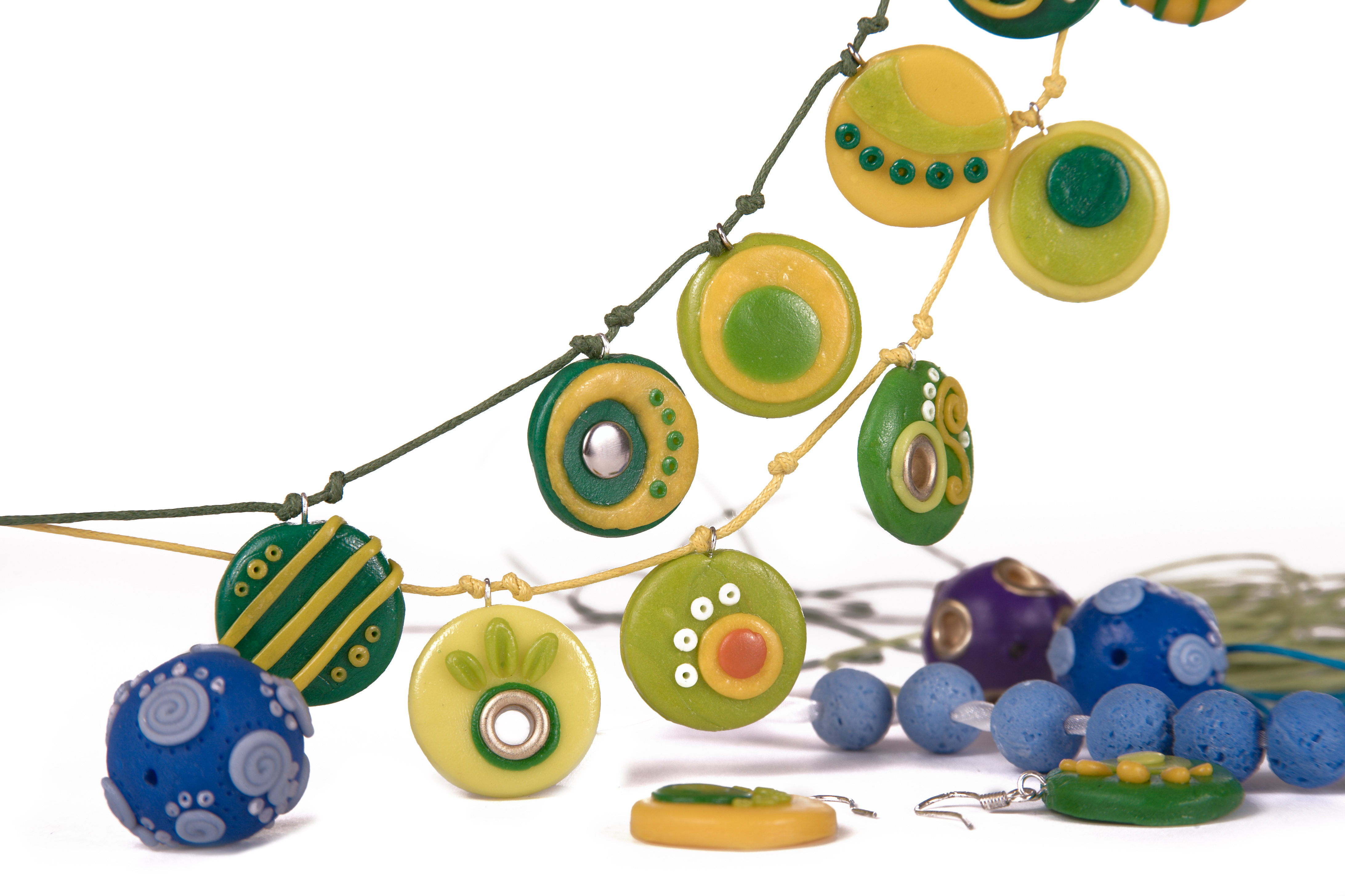 KI generiert: Das Bild zeigt eine Sammlung von buntem Schmuck, darunter Halsketten und Ohrringe mit runden, farbenfrohen und gemusterten Anhängern in Grün-, Gelb- und Blautönen. Im Vordergrund sind auch einige Perlen und ein Ohrhaken sichtbar.