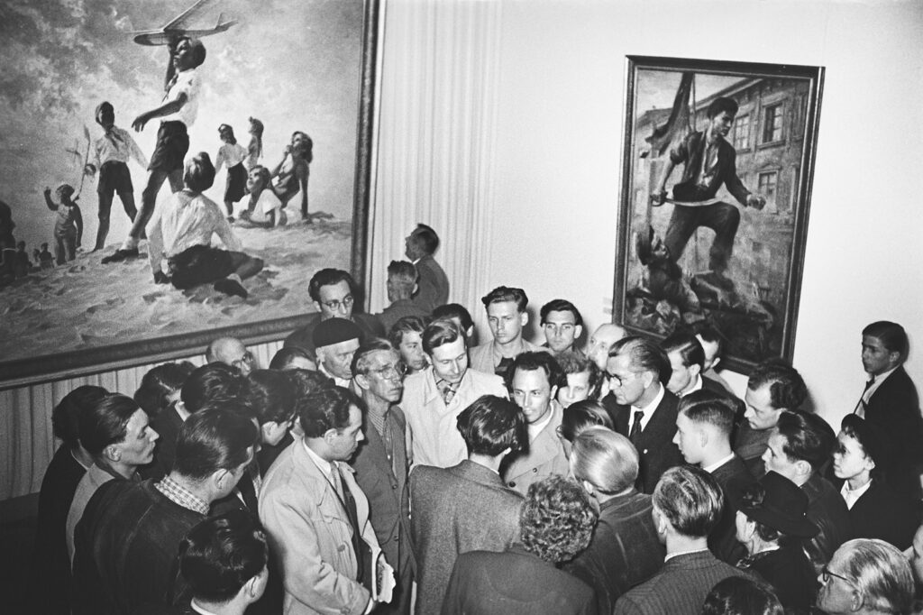KI generiert: Das Bild zeigt eine Gruppe von Menschen, die sich um zwei große Gemälde versammelt haben, vermutlich in einer Ausstellung. Die Gemälde scheinen Szenen mit Personen zu zeigen, die unterschiedliche Aktivitäten ausführen.