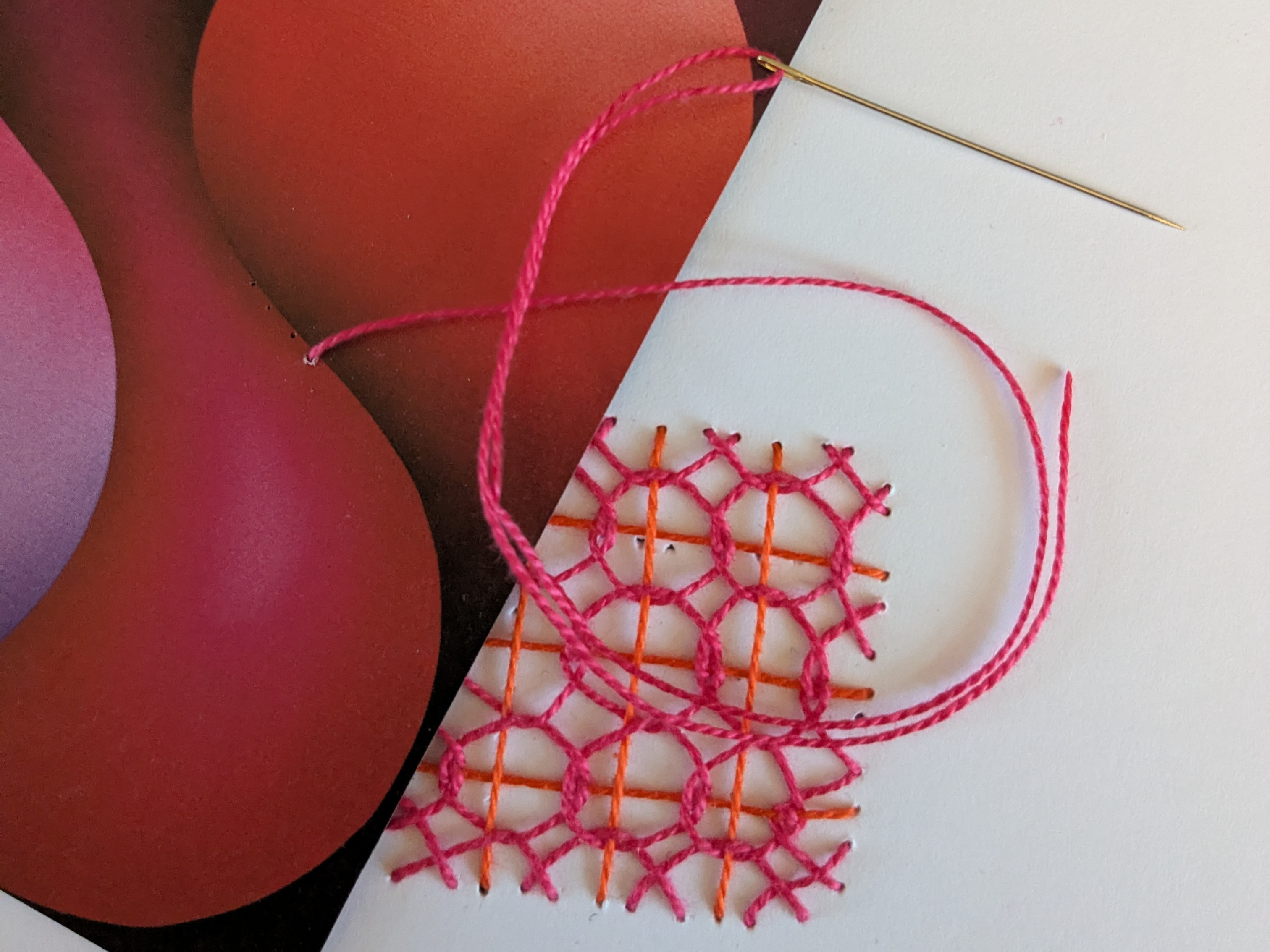 KI generiert: Das Bild zeigt eine Stickarbeit mit pinkfarbenem Garn auf einem geometrischen Muster neben einem Bild mit abstrakten, runden Formen in Rot- und Lilatönen. Eine Nadel ist in das Garn eingefädelt und liegt ebenfalls auf dem Muster.