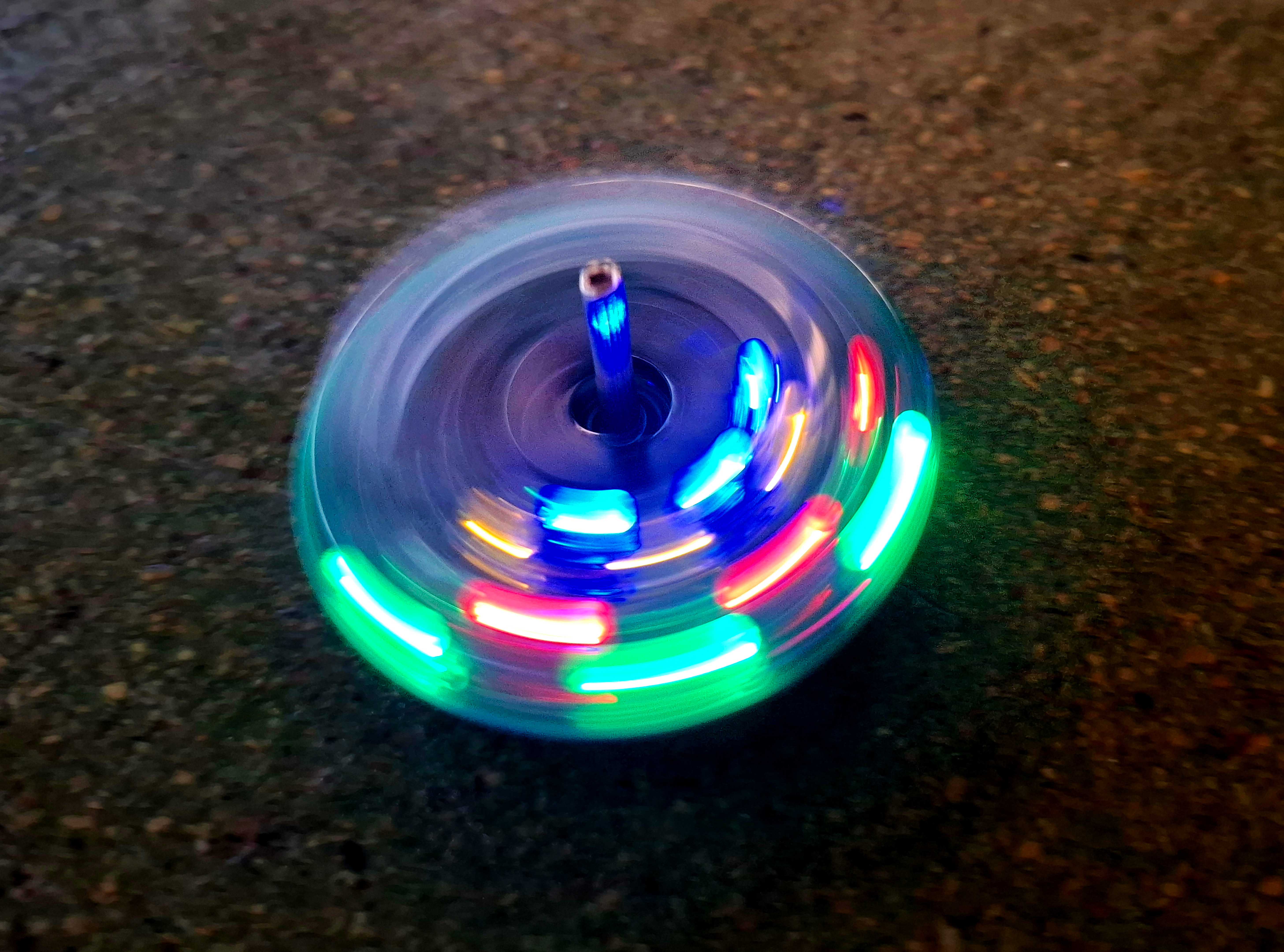 KI generiert: Das Bild zeigt einen sich drehenden Kreisel mit leuchtenden LED-Lichtern in verschiedenen Farben. Der Kreisel erzeugt durch seine Rotation einen bunten Leuchteffekt.