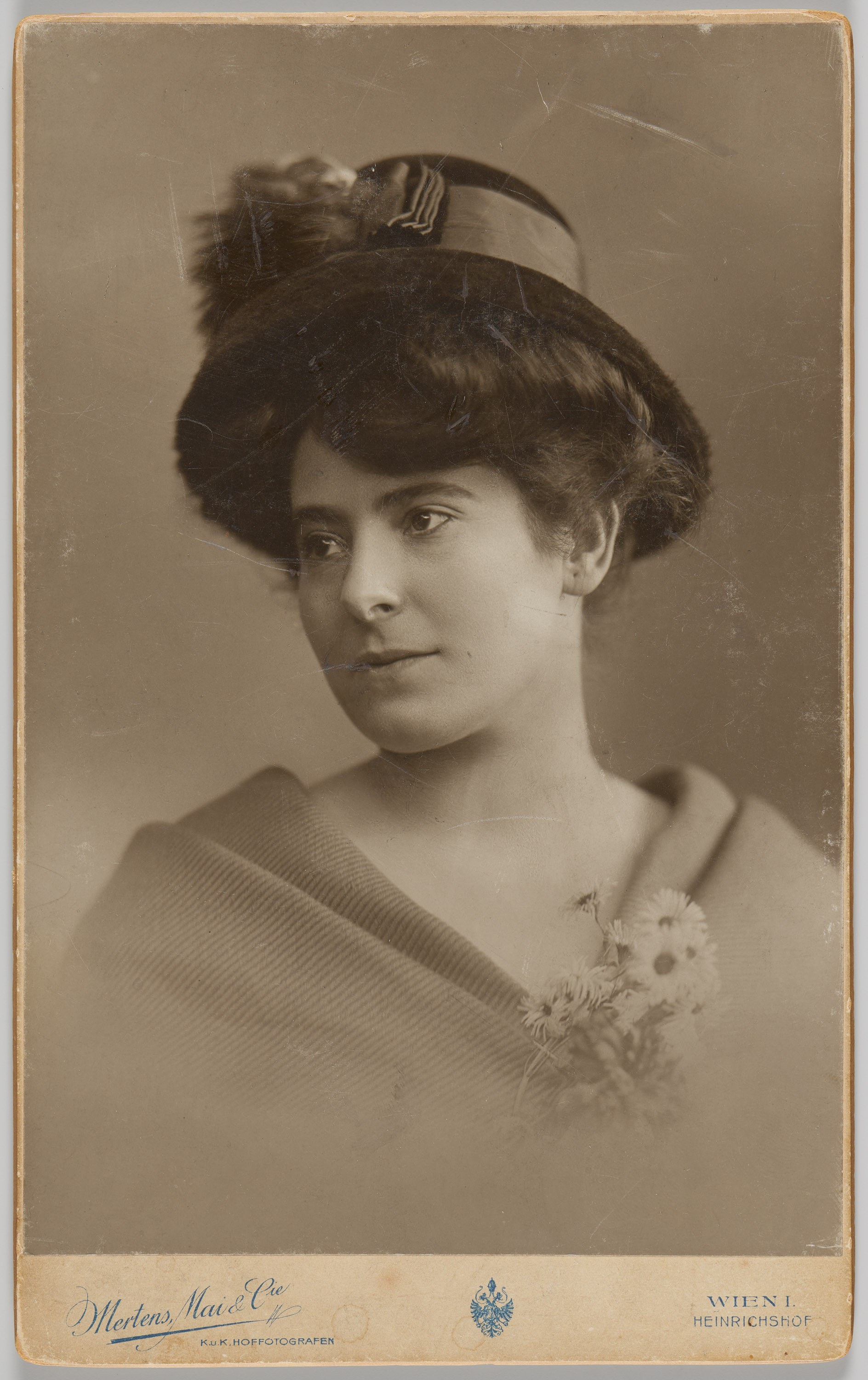 AI generated: The image shows a woman in a historical portrait, dressed in a hat and a cloak or scarf, while looking to the side. She is holding a small bouquet of flowers in her hand.