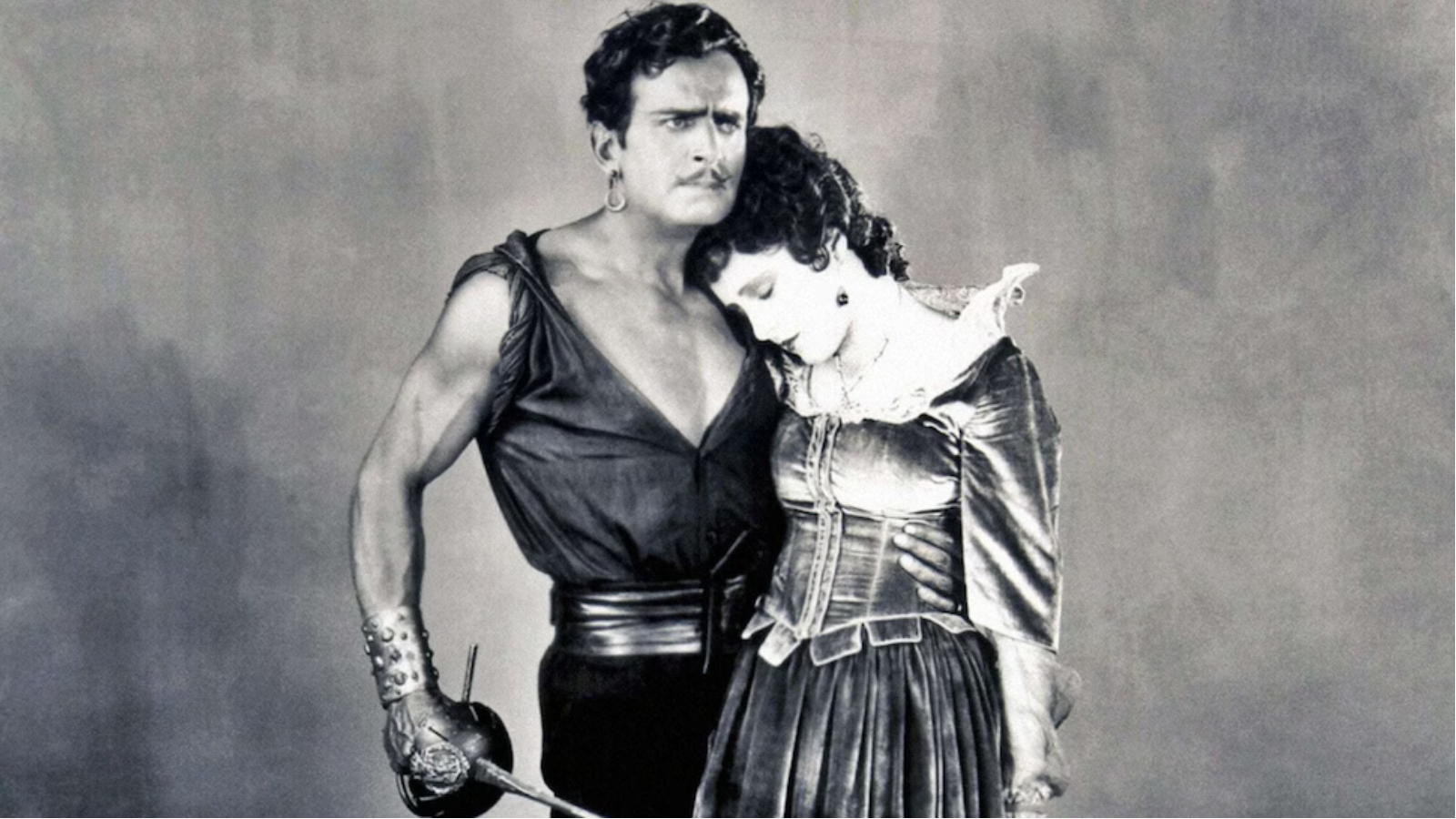 KI generiert: Das Bild zeigt ein historisch anmutendes Paar in einem Schwarz-Weiß-Stil, wobei der Mann einen Degen hält und die Frau sich an ihn lehnt. Beide tragen Kostüme, die an eine vergangene Epoche erinnern, möglicherweise aus einem Theaterstück oder Film.