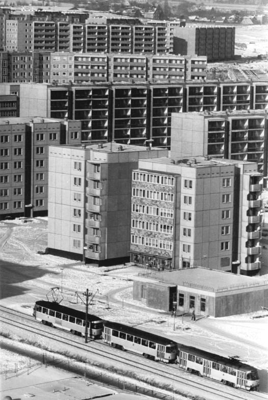AI generated: The image shows an urban residential neighbourhood with prefabricated high-rise buildings, which were typical in the GDR. In the foreground, a tram passes the apartment blocks.