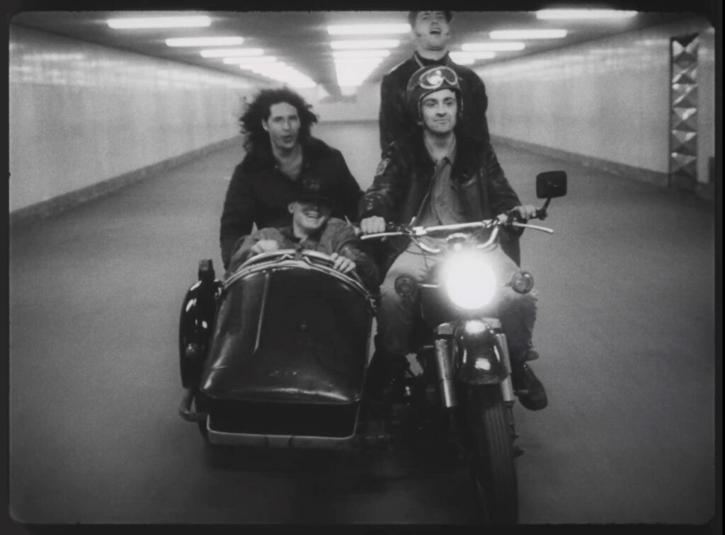 KI generiert: Das Bild zeigt drei Männer und ein Kind, die auf einem Motorrad mit Beiwagen durch einen Tunnel fahren. Alle wirken glücklich und es herrscht eine dynamische, fröhliche Atmosphäre.