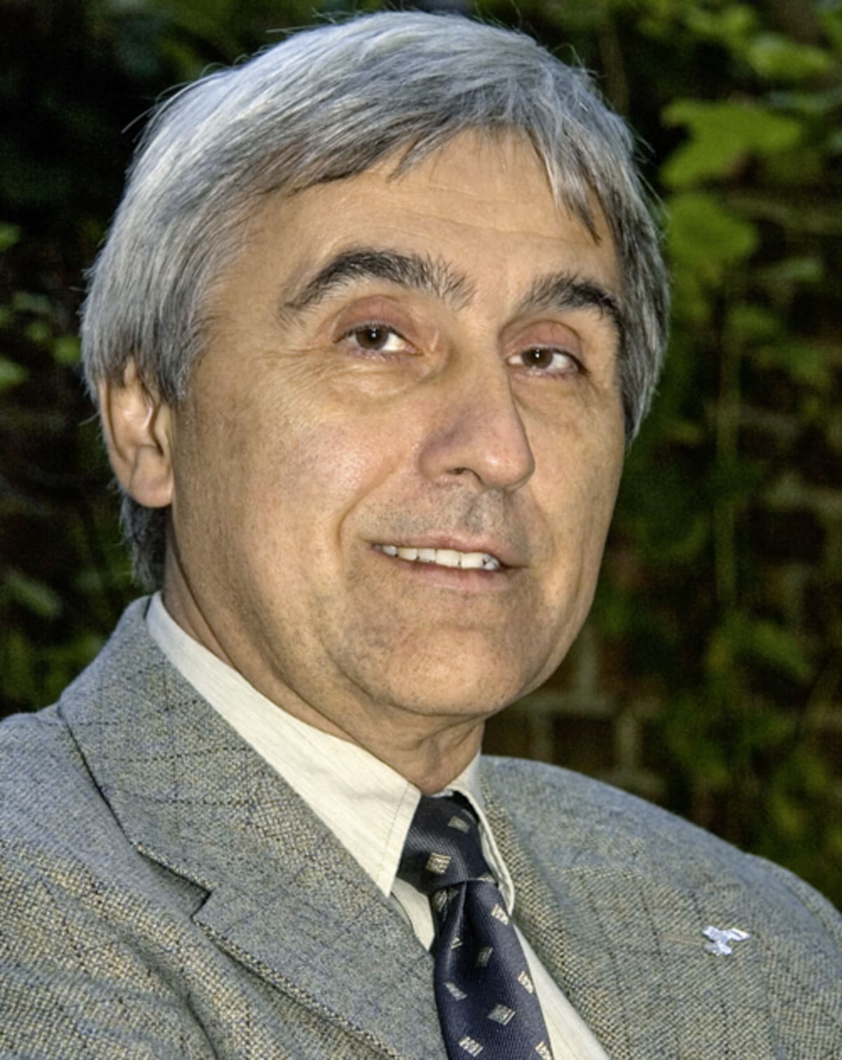 KI generiert: Das Bild zeigt eine Person in formeller Kleidung, bestehend aus einem grauen Sakko und einer Krawatte. Der Hintergrund ist grün und wirkt, als wäre er von Pflanzen bedeckt.