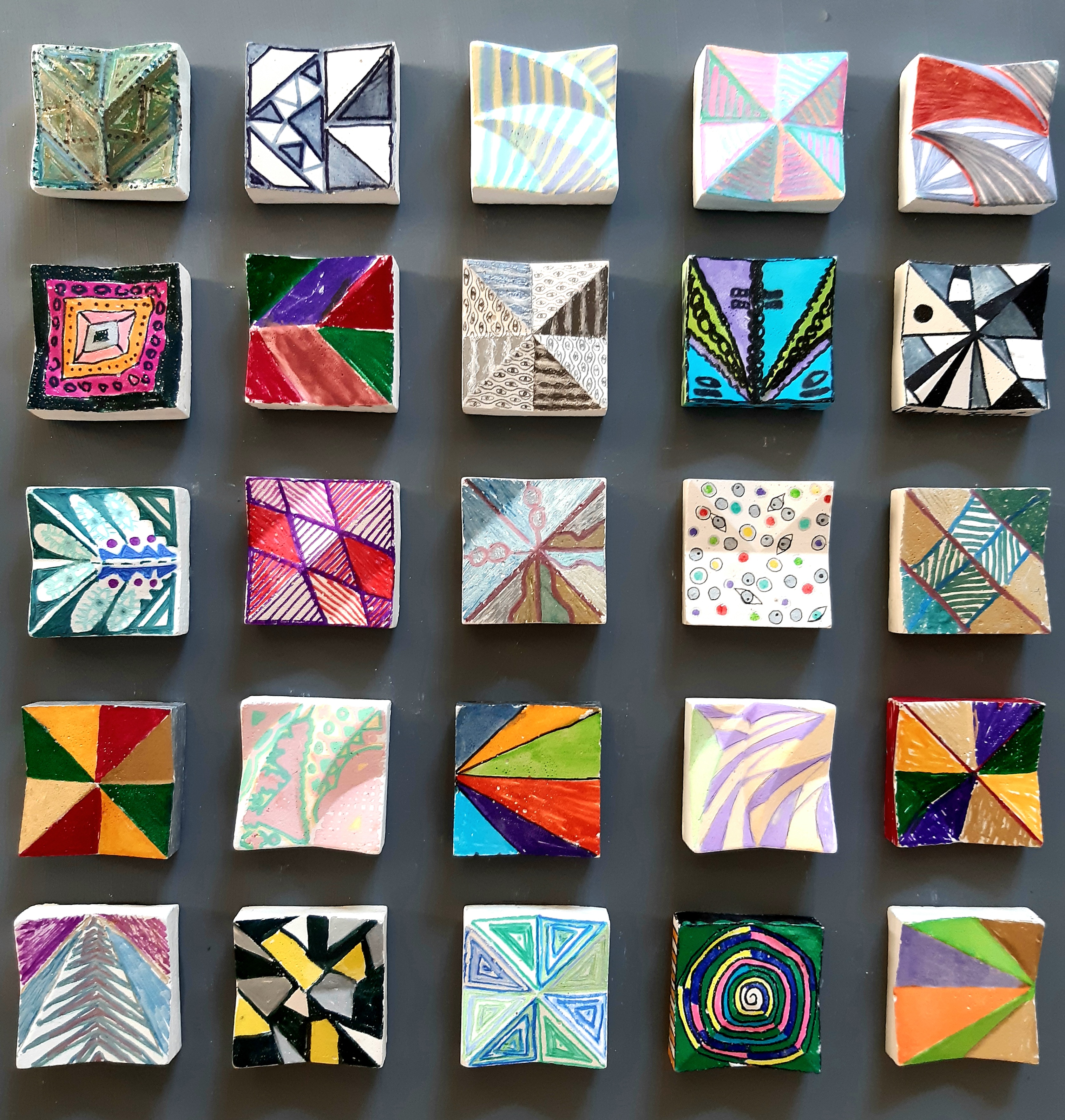 AI generated: The image shows an arrangement of 25 small, square tiles, each painted with different colourful and geometric patterns. The tiles are arranged evenly on a grey background.