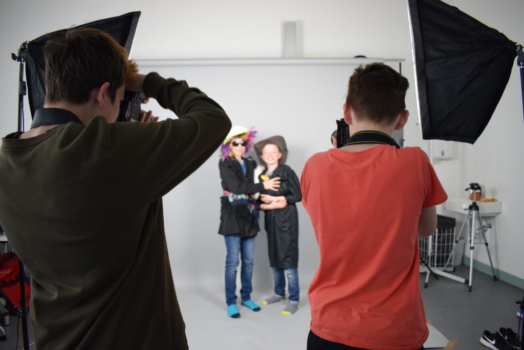 KI generiert: Das Bild zeigt eine Studioaufnahme, bei der zwei Personen in Kostümen posieren, während zwei Fotografen sie ablichten. Es handelt sich anscheinend um eine Fotosession oder ein Fotoshooting.