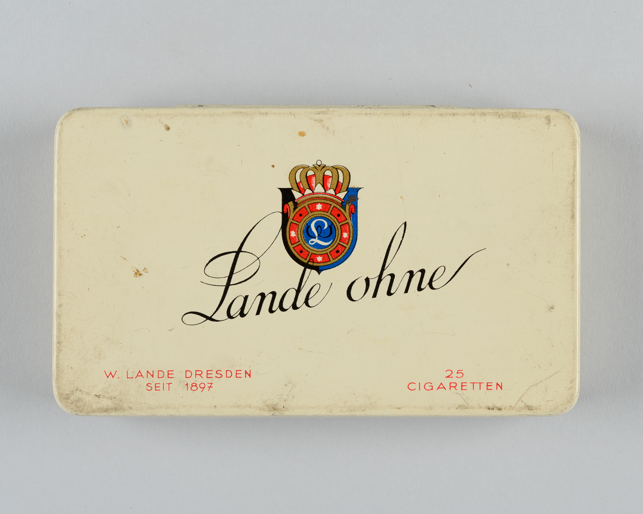 AI generated: The picture shows an old cigarette tin of the brand "Lande ohne" with a classic design and a decorative emblem in the centre. The tin is labelled "W. Lande Dresden, since 1897" and contains 25 cigarettes.