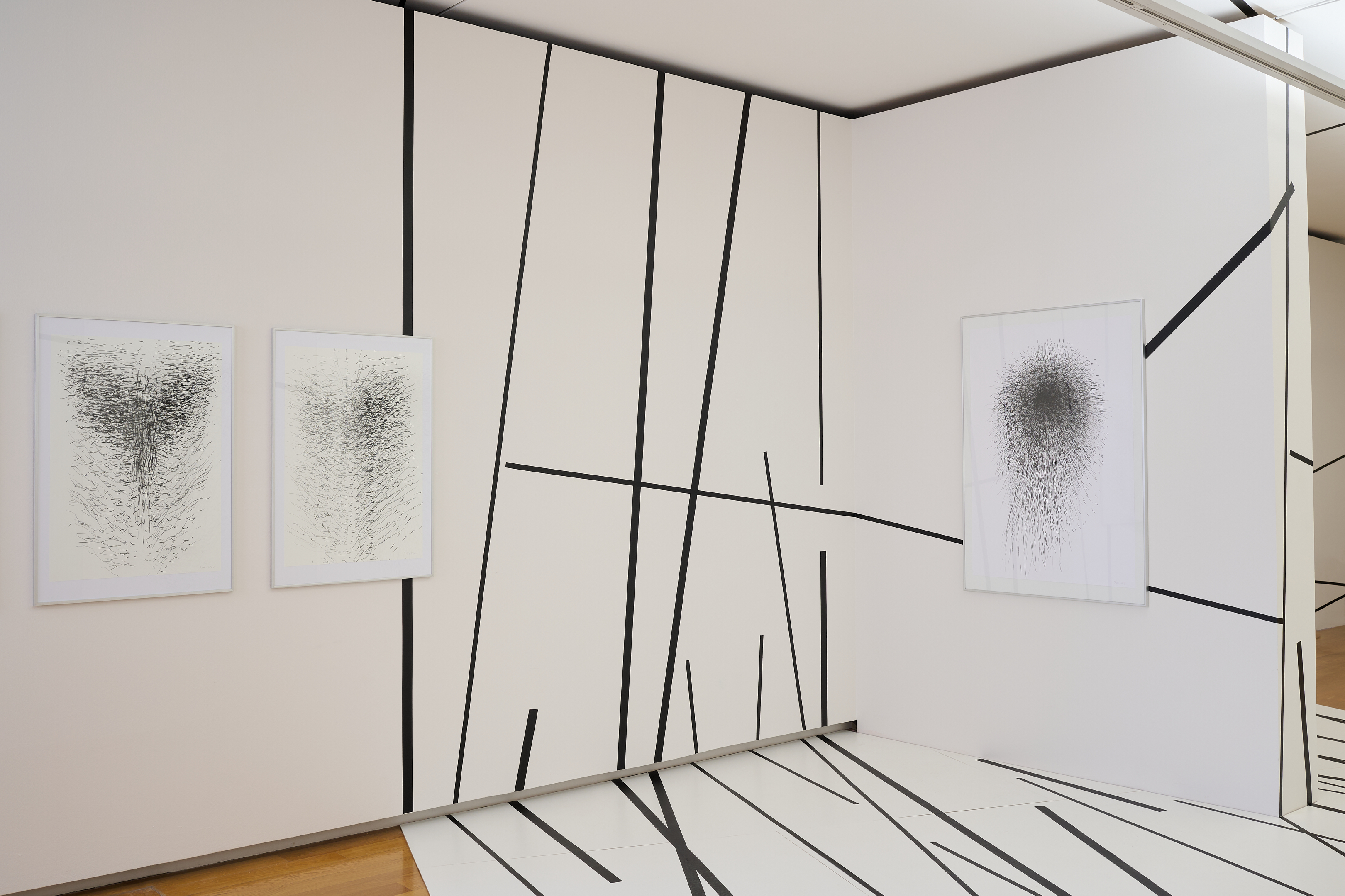 KI generiert: Das Bild zeigt eine Galerie mit einer Installation aus schwarzen Linien, die sich über Wände und Boden erstrecken, sowie drei gerahmten Kunstwerken mit chaotischen schwarzen Linienmustern. Der Raum erzeugt einen dreidimensionalen Effekt, der die Grenzen zwischen Kunstwerk und Umgebung verschwimmen lässt.