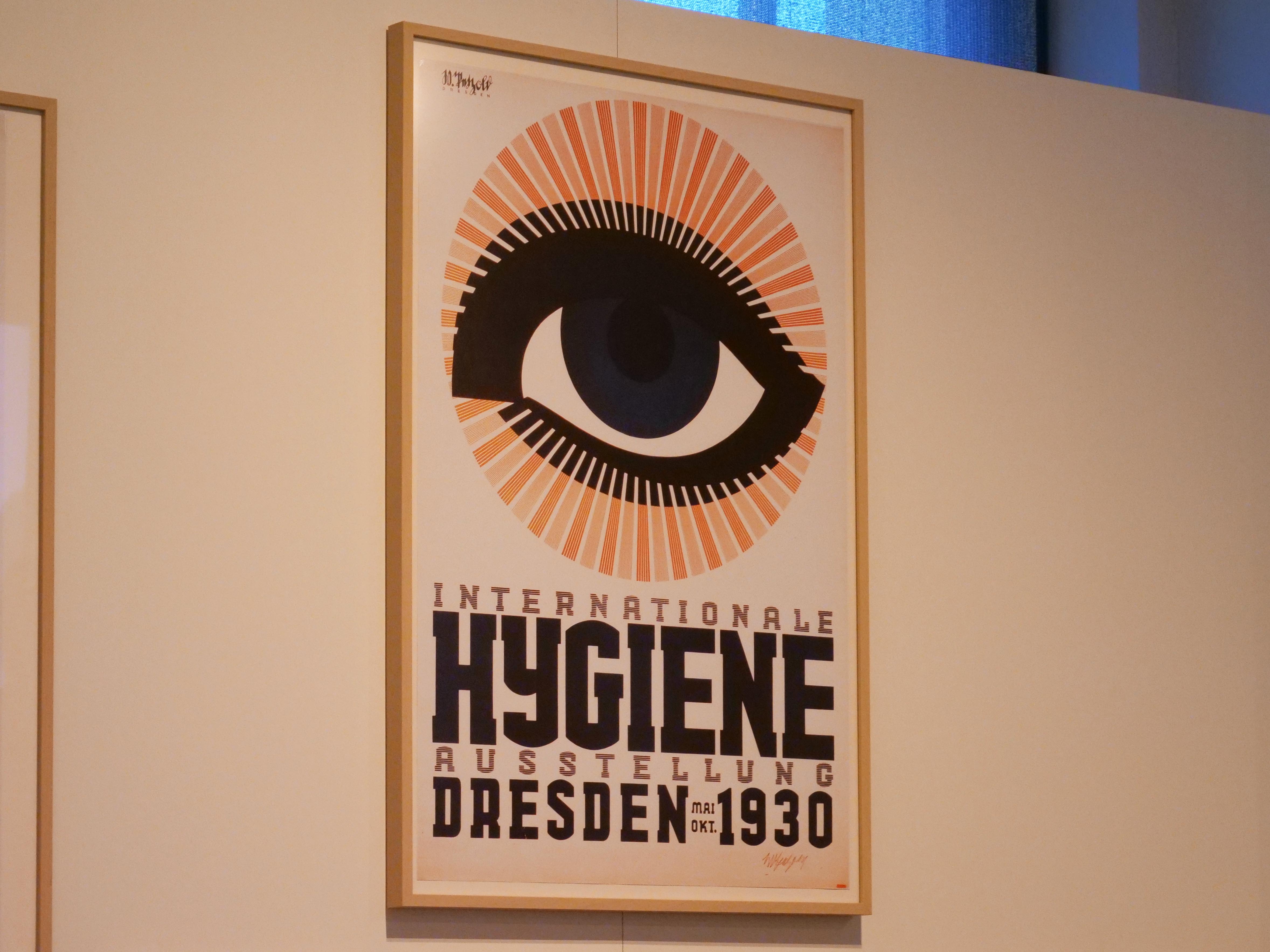 KI generiert: Das Bild zeigt ein Plakat der Internationalen Hygiene-Ausstellung in Dresden im Jahr 1930. Es hebt sich durch ein großes, stilisiertes Auge über der Schrift hervor.