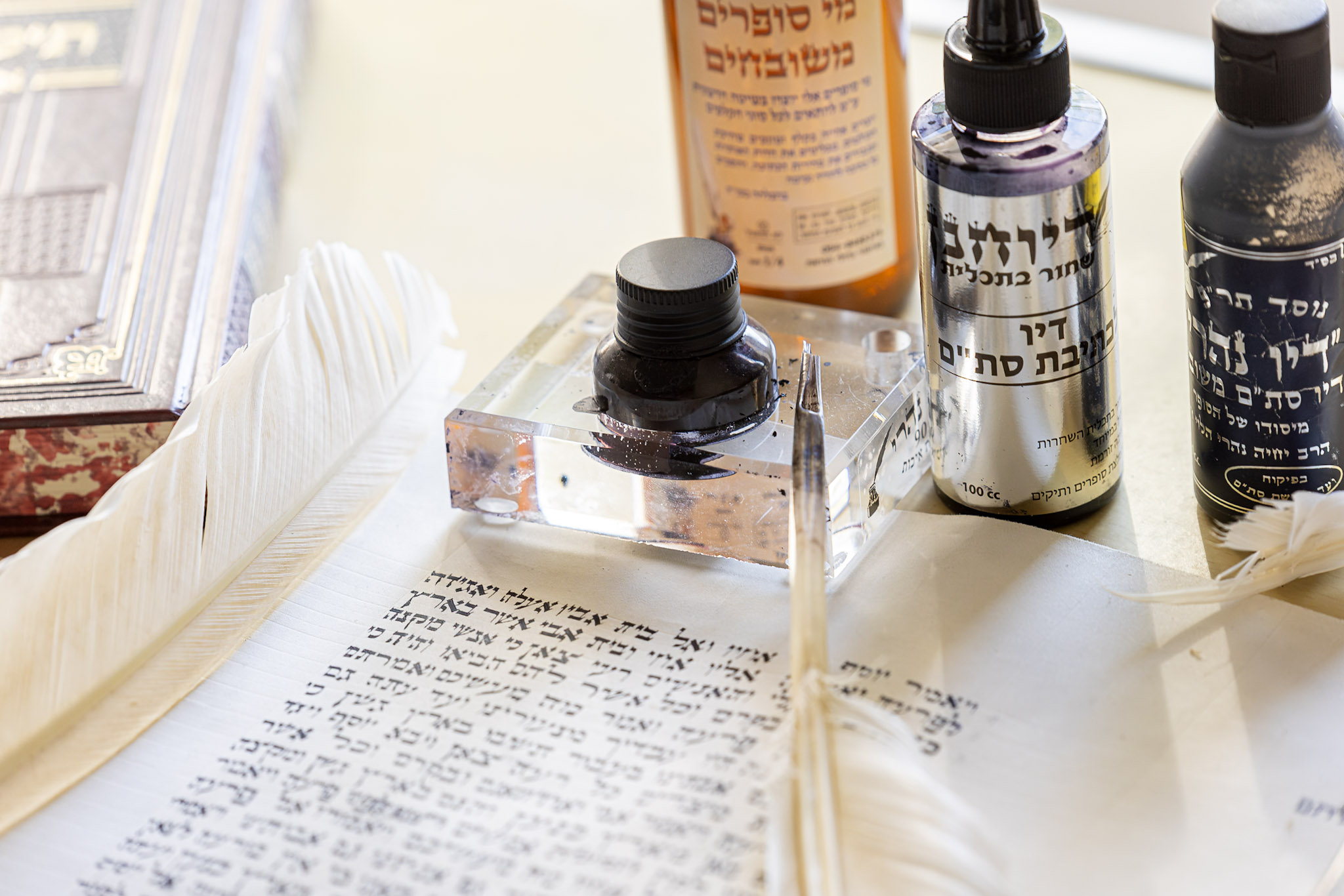 KI generiert: Das Bild zeigt traditionelle Schreibutensilien, darunter Tintenflaschen und Schreibfedern, die zusammen mit einem beschrifteten Text in hebräischer Schrift arrangiert sind. Der Fokus liegt auf der künstlerischen und traditionellen Kalligraphie.